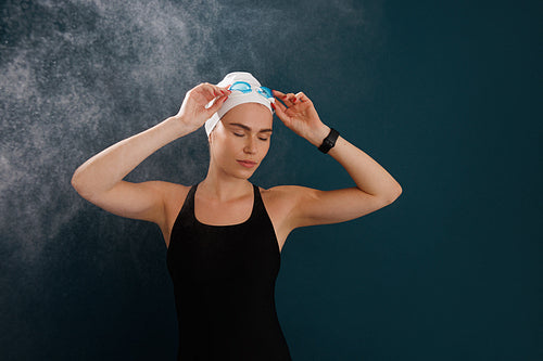 Young woman swimmer with closed eyes adjusting her swimming goggles