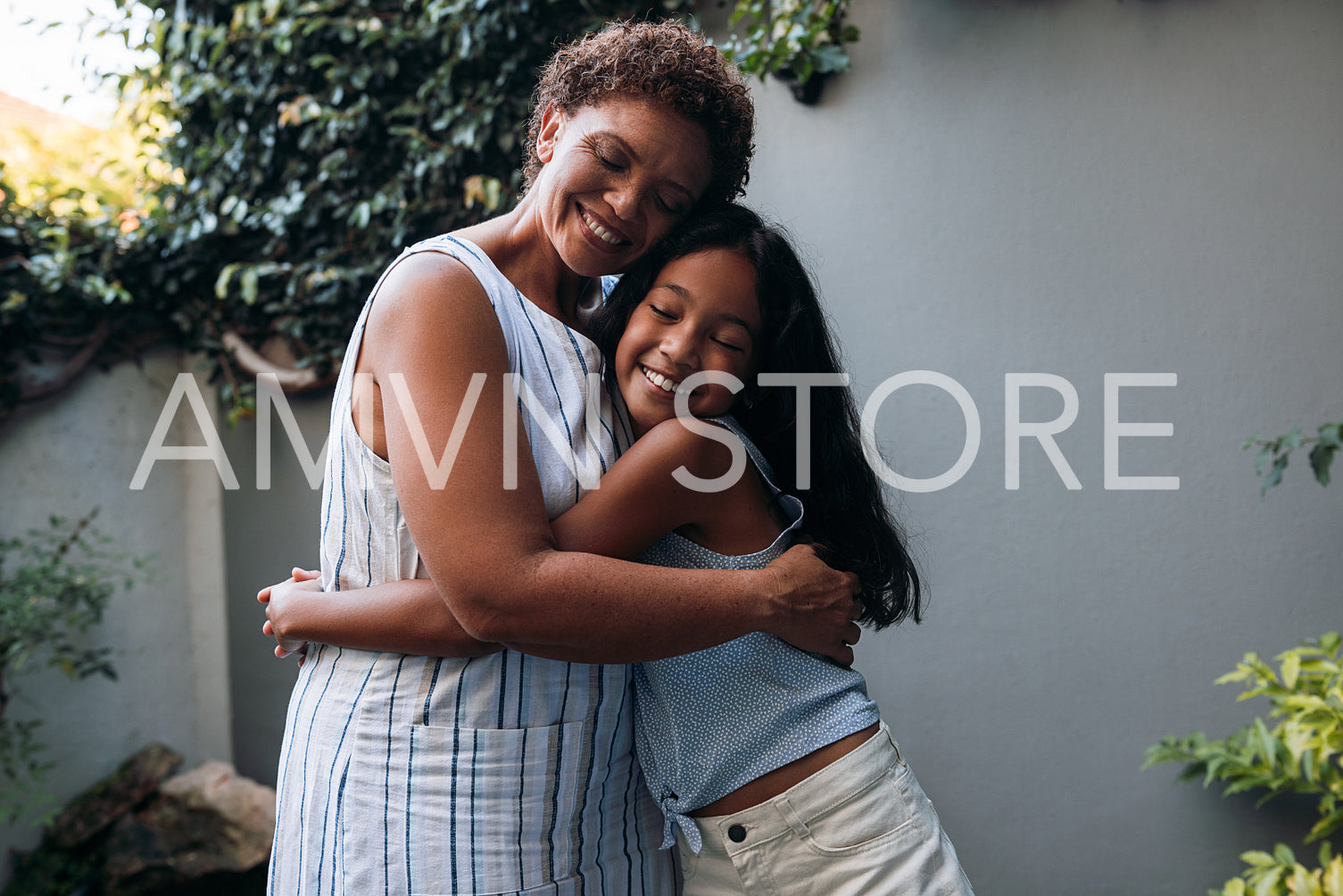 Smiling girl hugging her granny in the backyard. Grandmother and granddaughter are embracing with closed eyes.