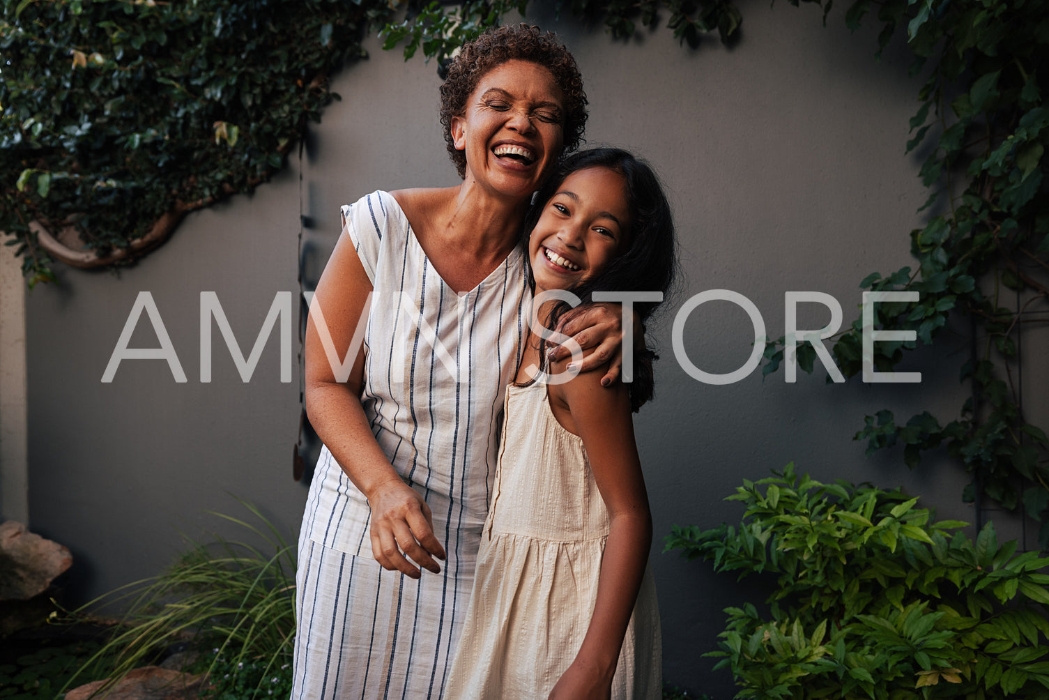 Portrait of granny and granddaughter embracing and laughing. Happy grandmother and kid standing together in backyard.