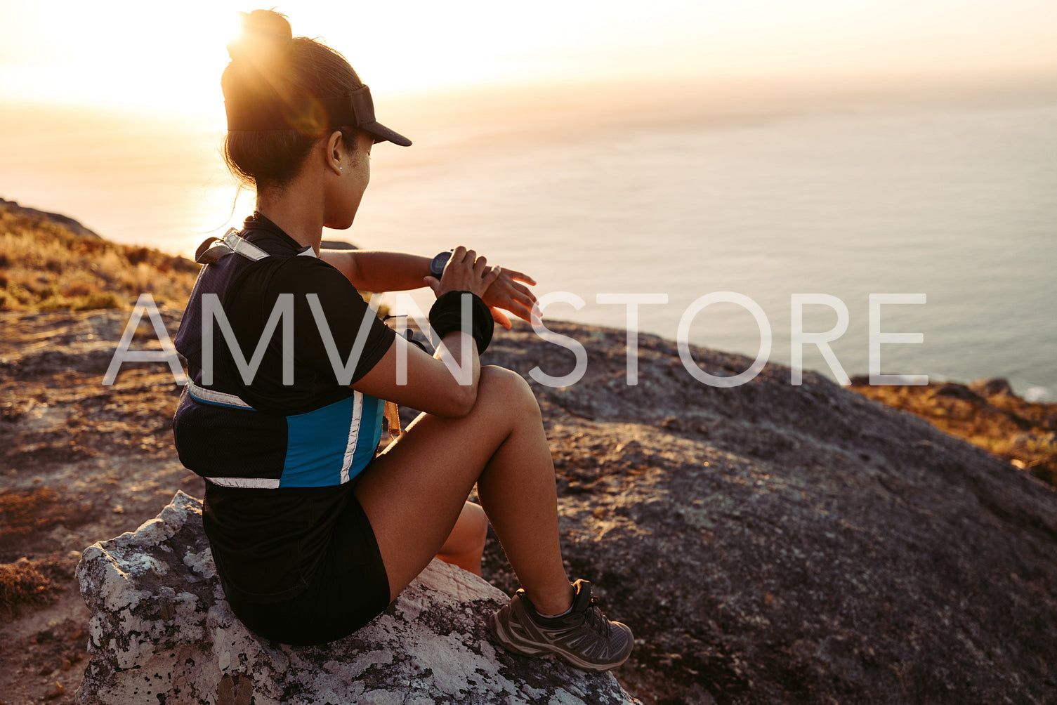 Woman hiker sitting on a rock on the top of the mountain checking smartwatch. Female in sportswear on a hill at sunset.