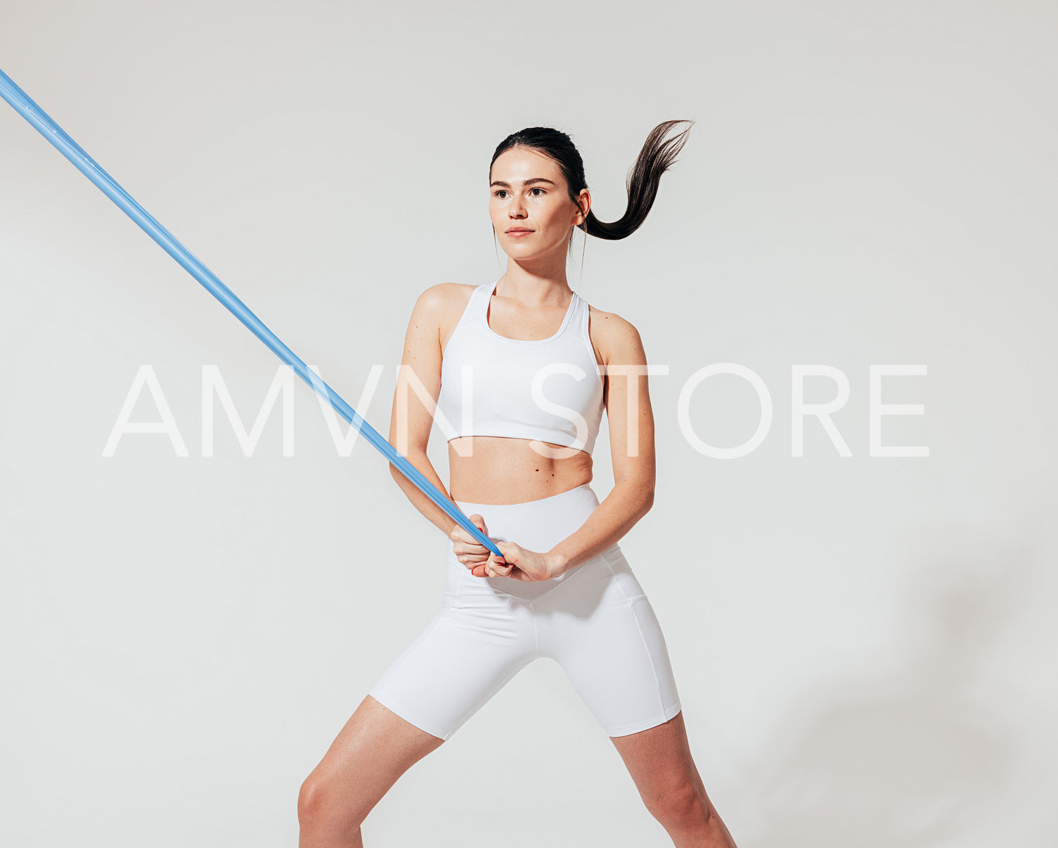 Healthy slim woman in white sports clothes practicing with resistance band in studio