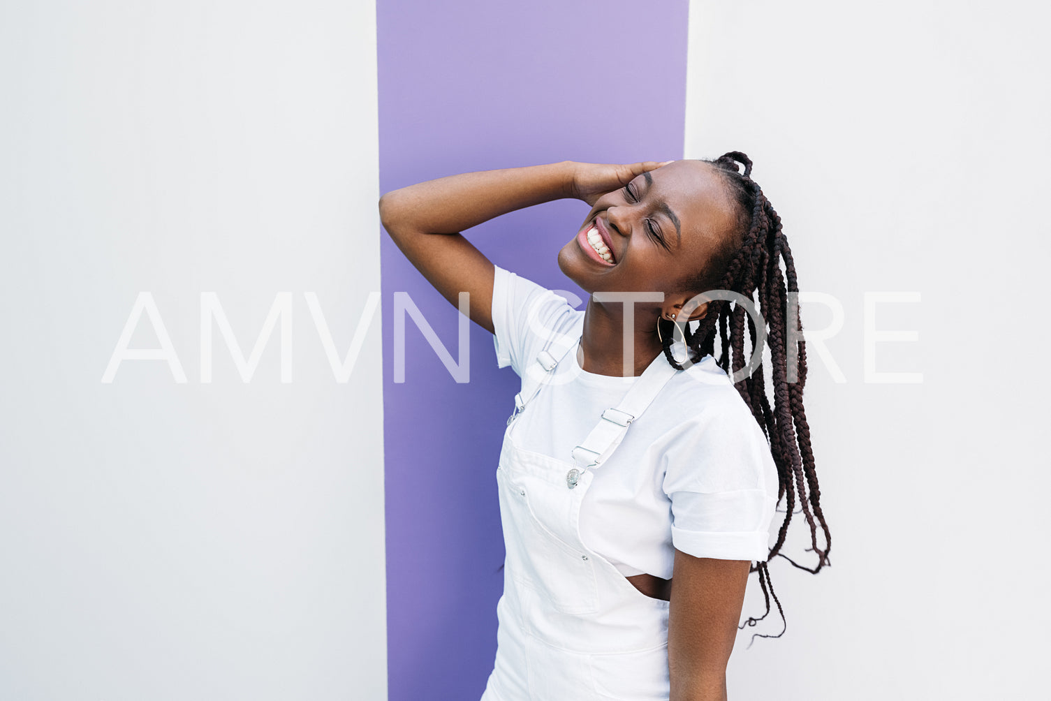 Happy woman with closed eyes wearing white clothes leaning on white wall with purple stripe