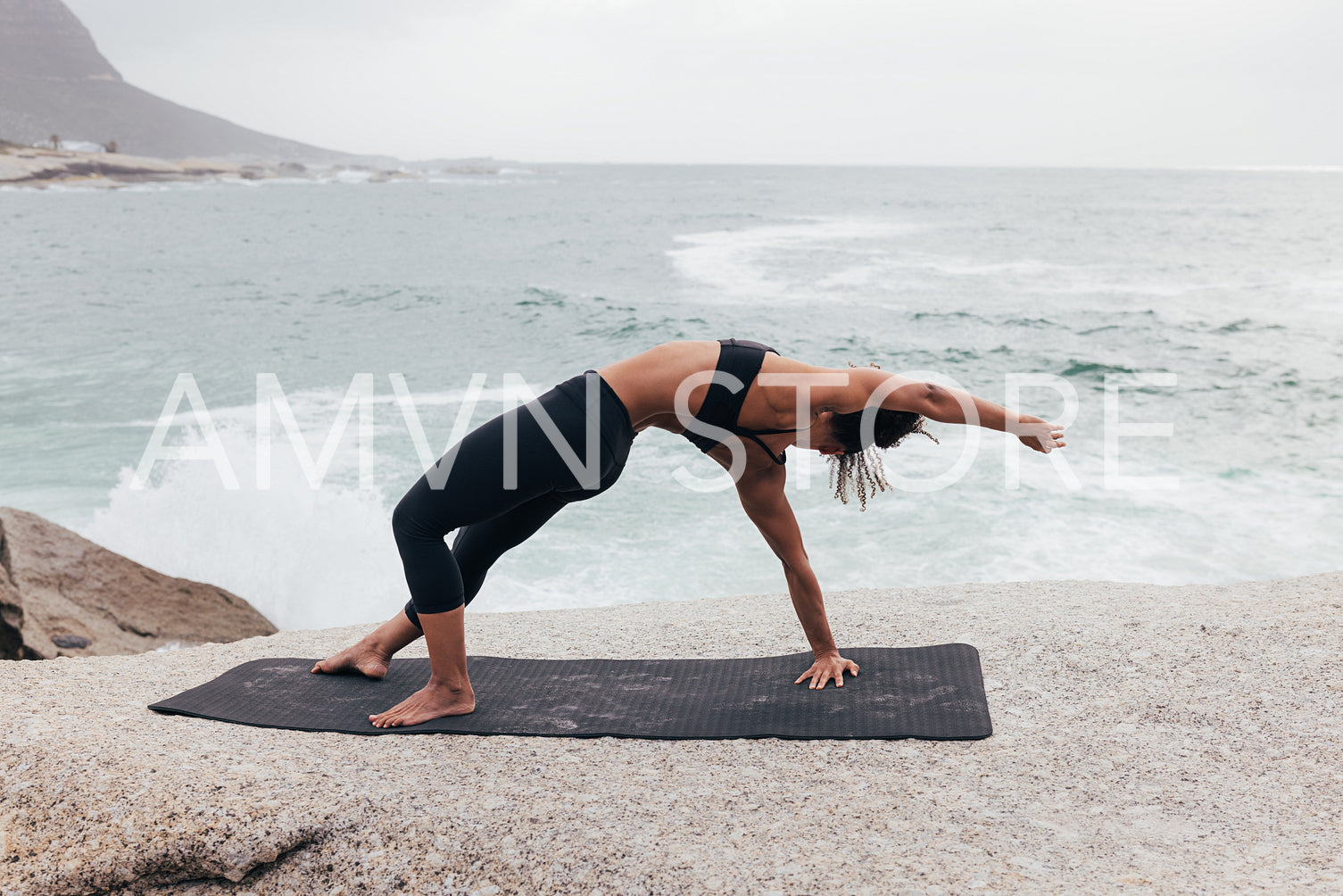 Slim female practicing yoga pose by ocean at coast