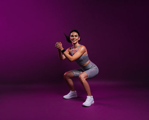 Young smiling woman in silver fitness attire doing sit-ups on a magenta background