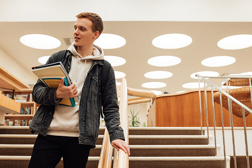 University student holding books going down the stairs in library