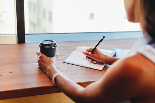 Unrecognizable freelance woman writing in notebook at cafe