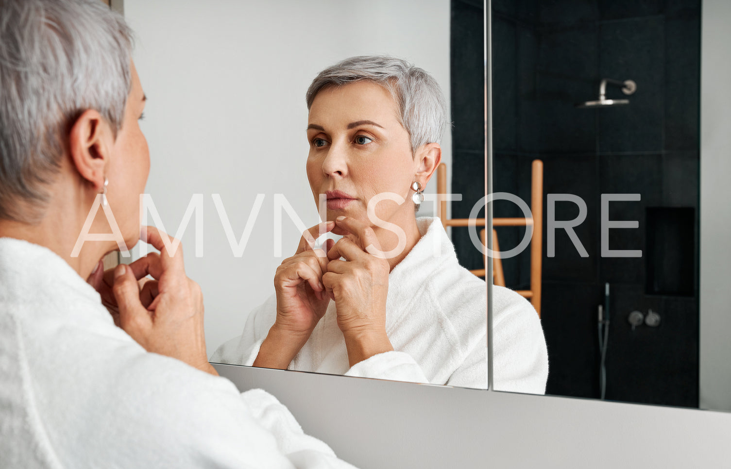 Senior woman spending time at home standing in bathroom looking in a mirror 