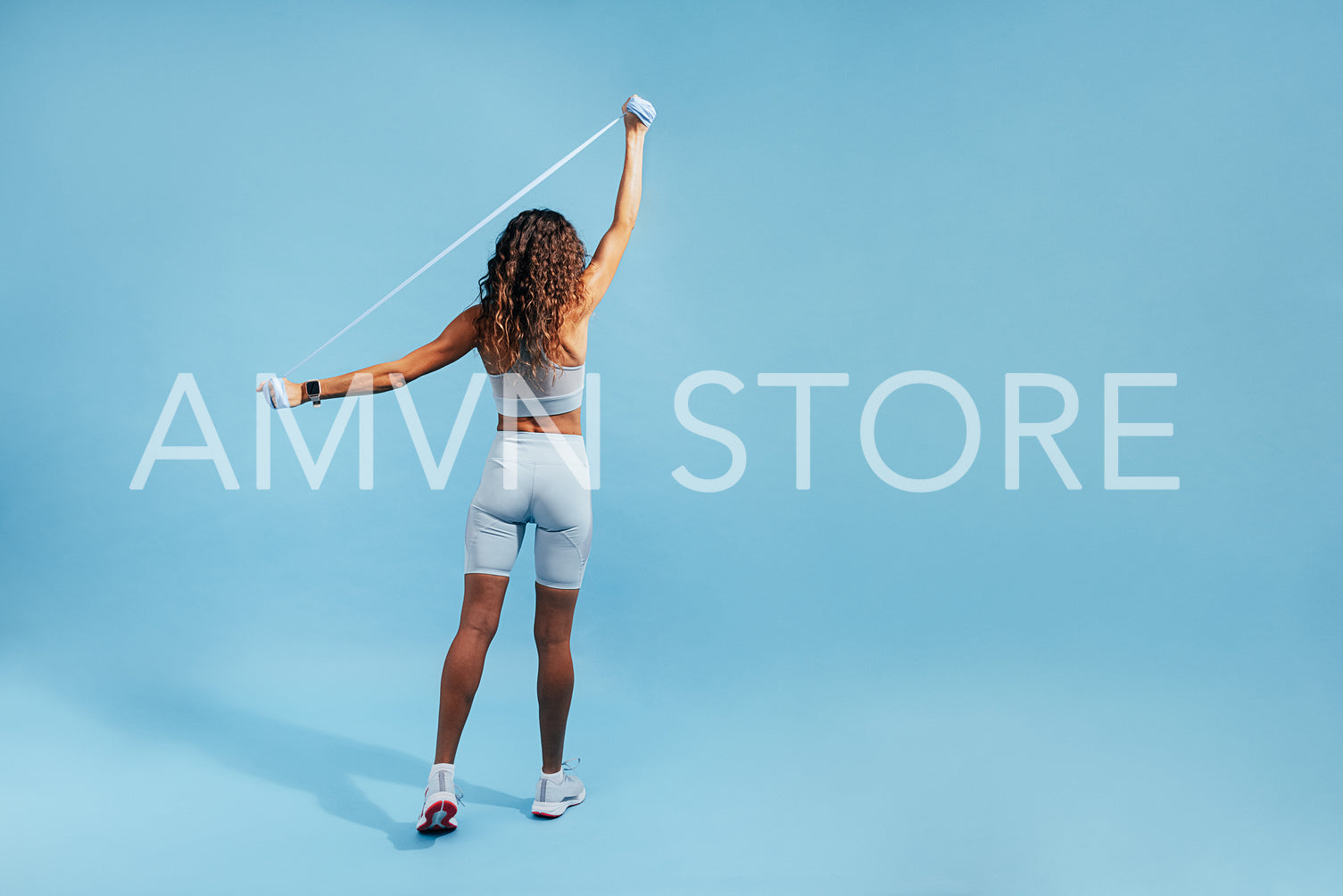 Rear view of female in sportswear using elastic band on blue background