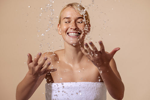 Happy woman wrapped in white towel splashing water on face in st