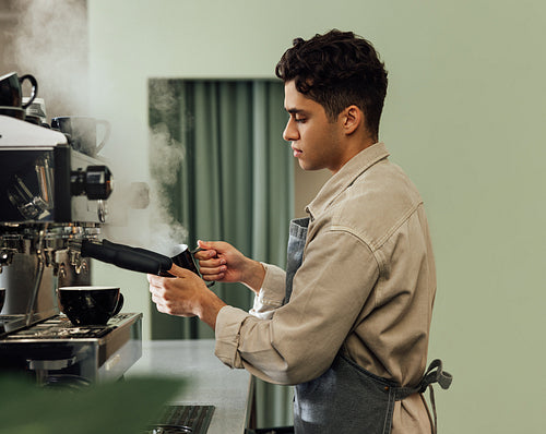 Side view of a male barista in an apron using a coffee machine. Barista using preparing cappuccino.