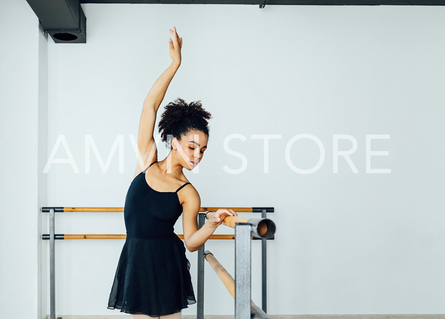 Young beautiful ballerina practicing ballet moves at barre in small studio	