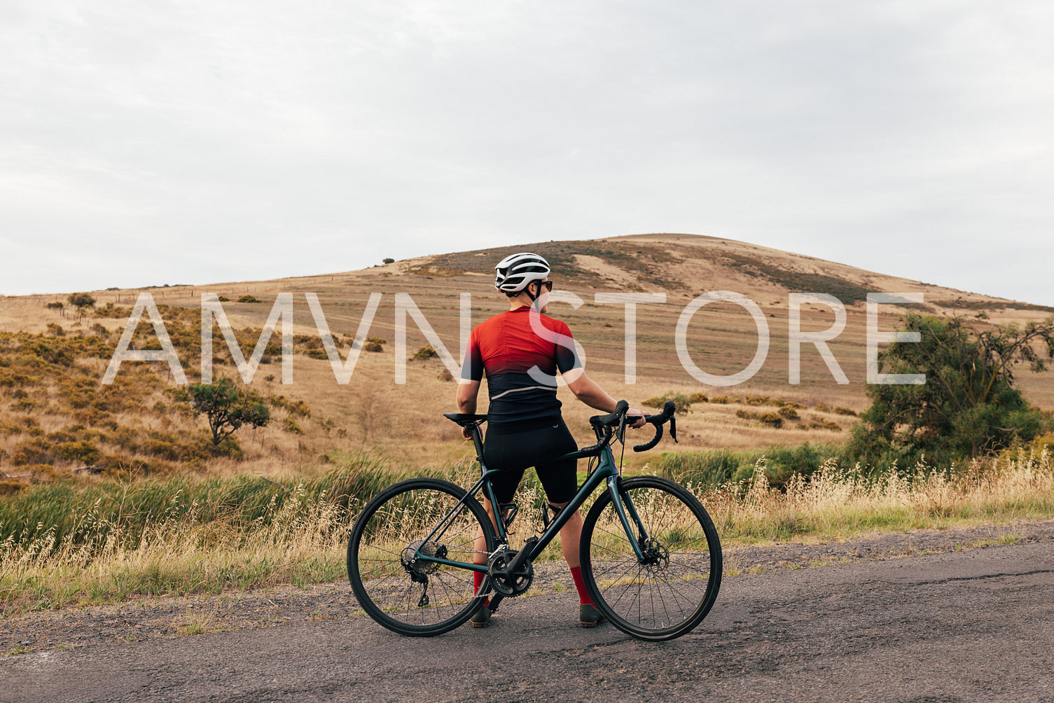 Back view of female cyclist taking break leaning on bike on empty country road