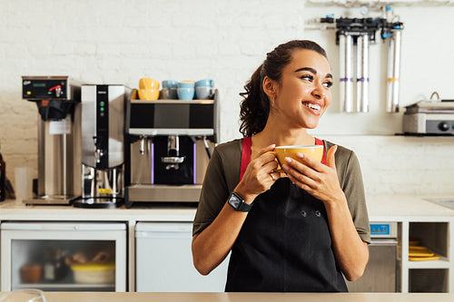 Female waitress holding coffee mug while standing at table in coffee shop