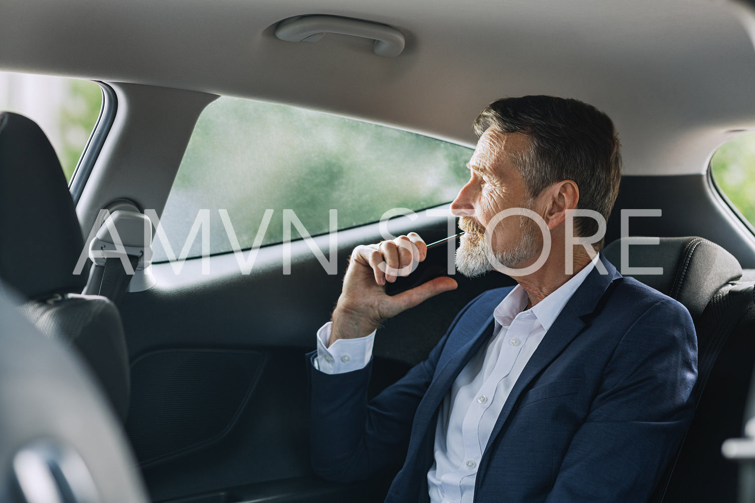 Businessman holding a cell phone in the car while looking thoughtfully out of a window	