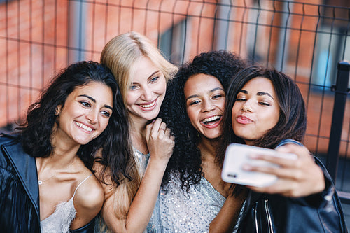 Group of happy female friends making photographs on smartphone outdoors