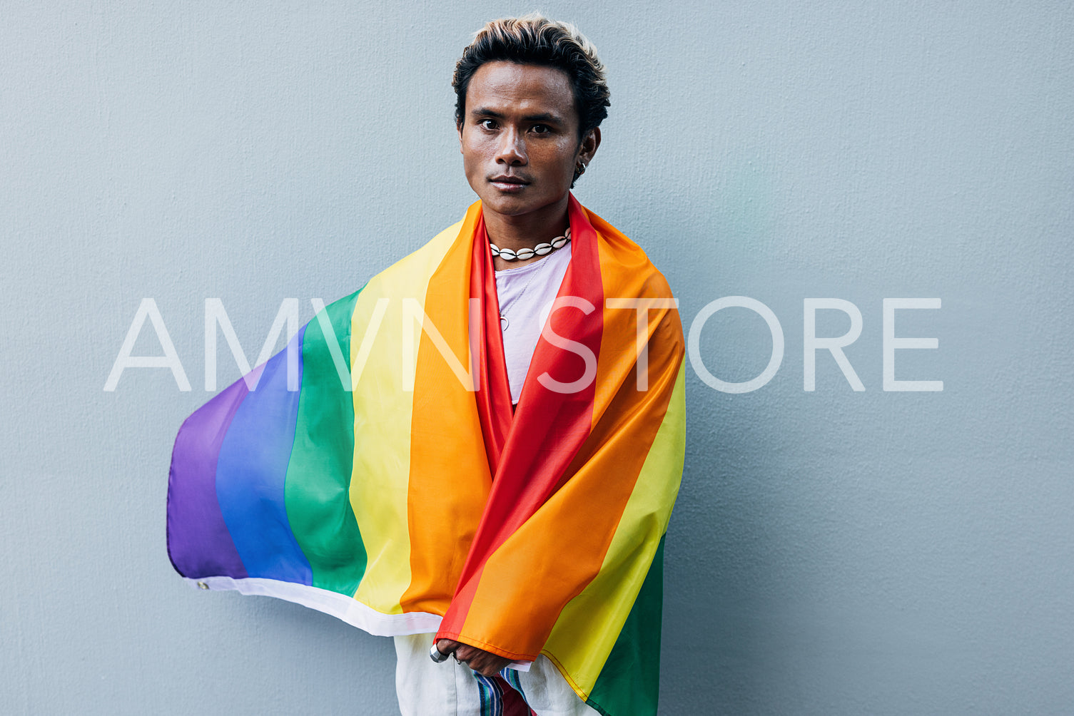 Young man wrapped in rainbow LGBT flag standing at grey wall outdoors