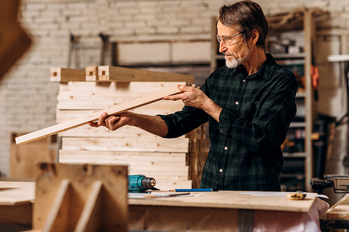 Male carpenter checking straightness of a wooden plank in workshop