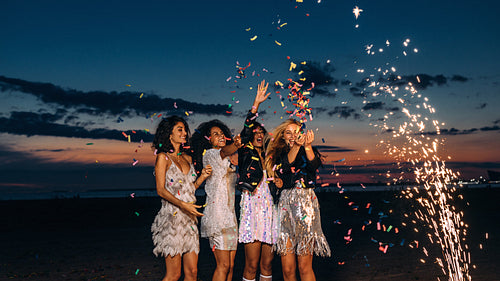 Four happy young female friends throwing confetti at sunset