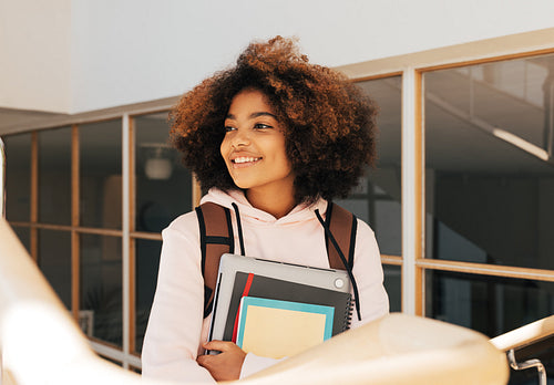 Smiling girl climbing college stairs. Student in university moving up the staircase and looking away.