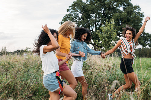 Laughing woman runs in front of her friends with a raised hand. Group of four young females on summer vacation.