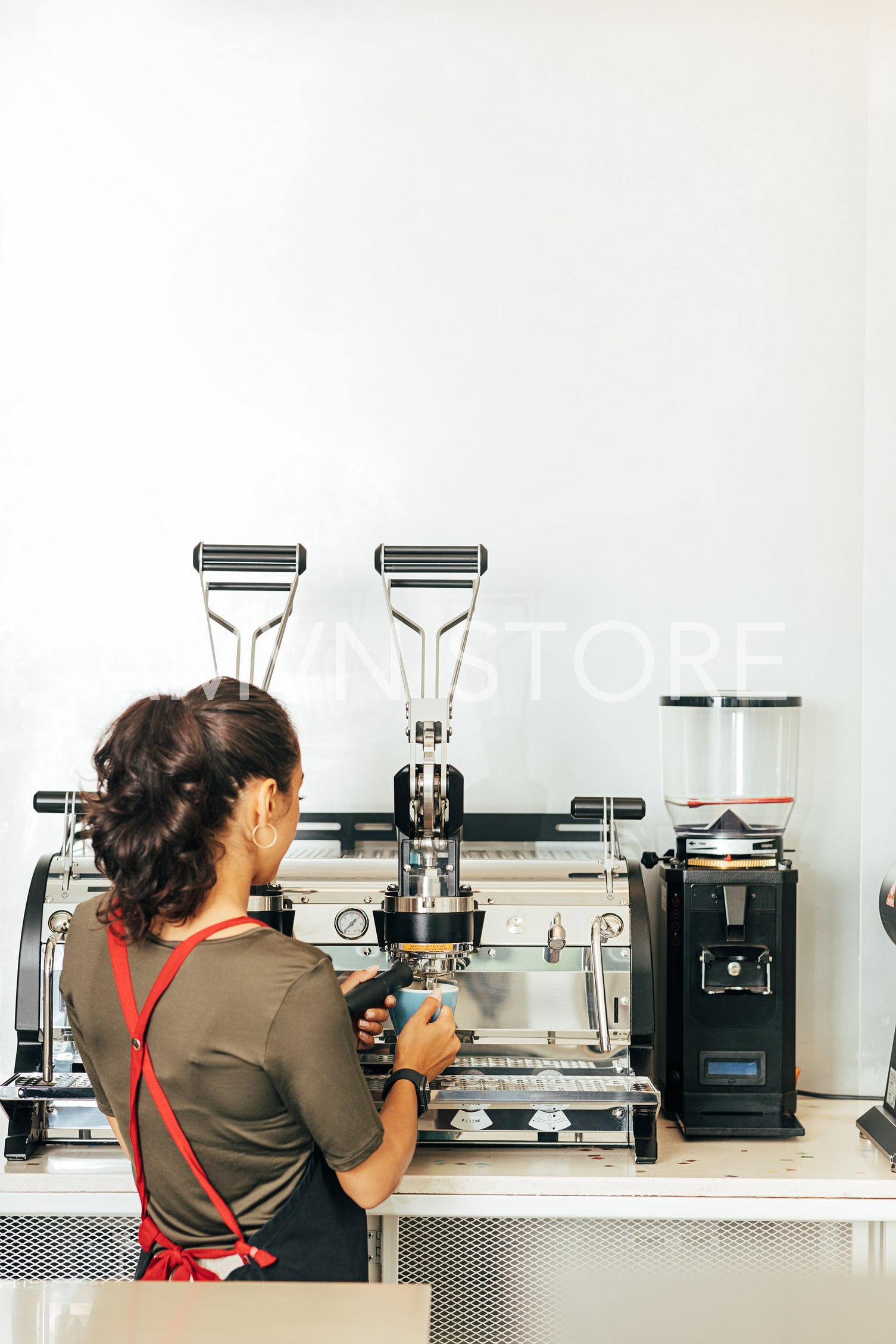 Back view of a female barista making coffee. Woman in apron working in a small coffee shop.	