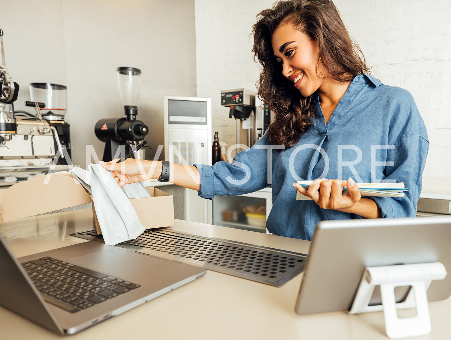 Young entrepreneur looking on pack of coffee and taking notes. Small cafe owner working at table with laptop and digital tablet.	