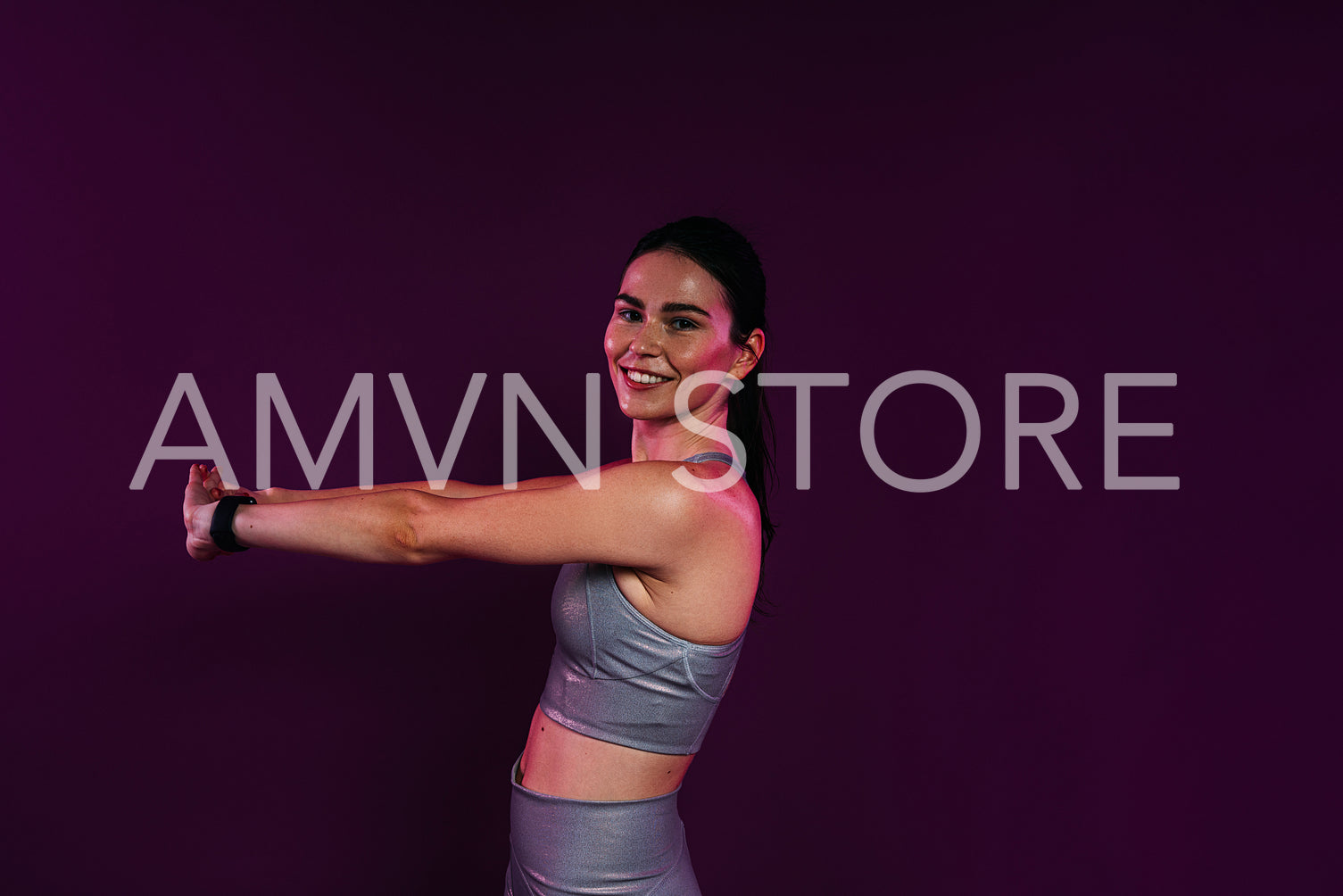 Side view of young smiling female stretching and flexing her hands over magenta background in studio