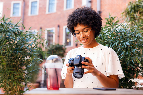 Young vlogger sitting at outdoor cafe and operating a digital camera