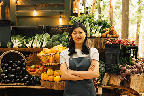 Portrait of a confident outdoor market employee. Smiling Asian woman in an apron standing at her outdoor stall.