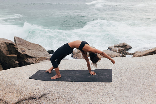 Slim female in yoga by ocean. Woman in fitness wear practicing yoga pose outdoors.