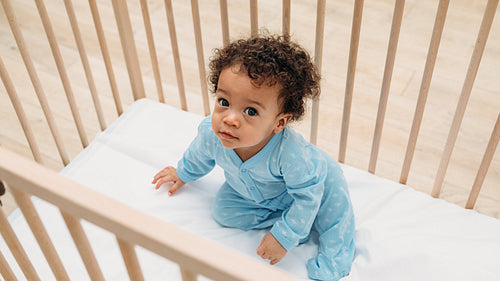 Portrait of cute baby boy sitting in crib at home