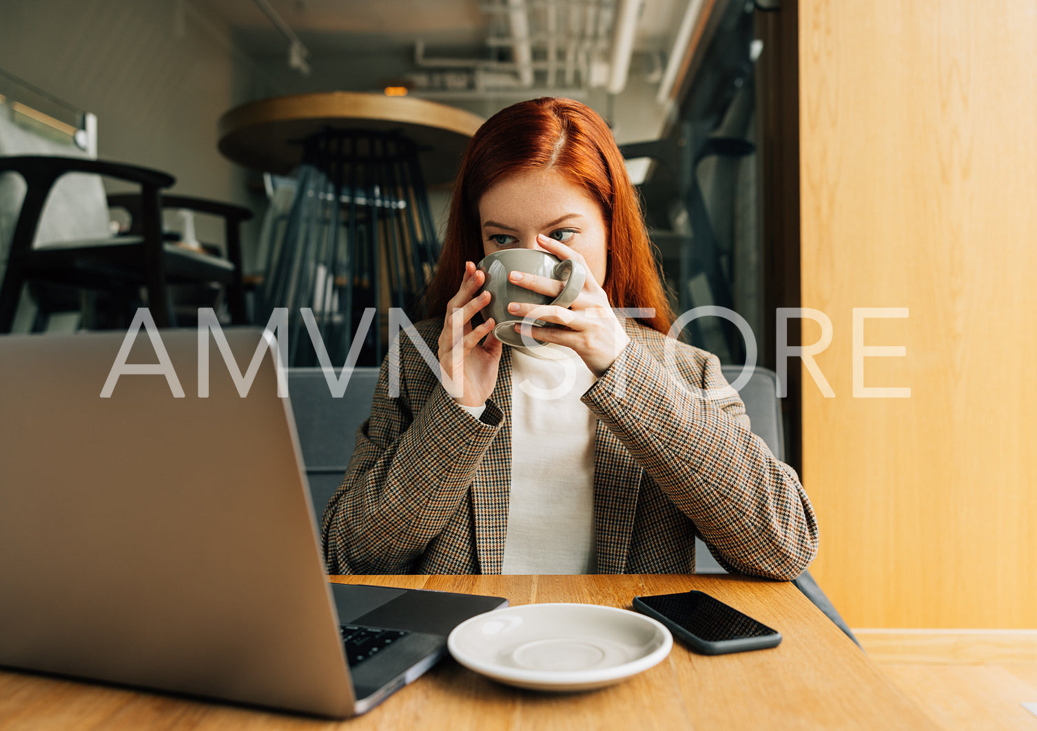 Woman drinking coffee and looking at laptop while sitting at a table in cafe