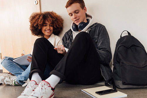 Two classmates preparing their assignments together while sitting on the floor