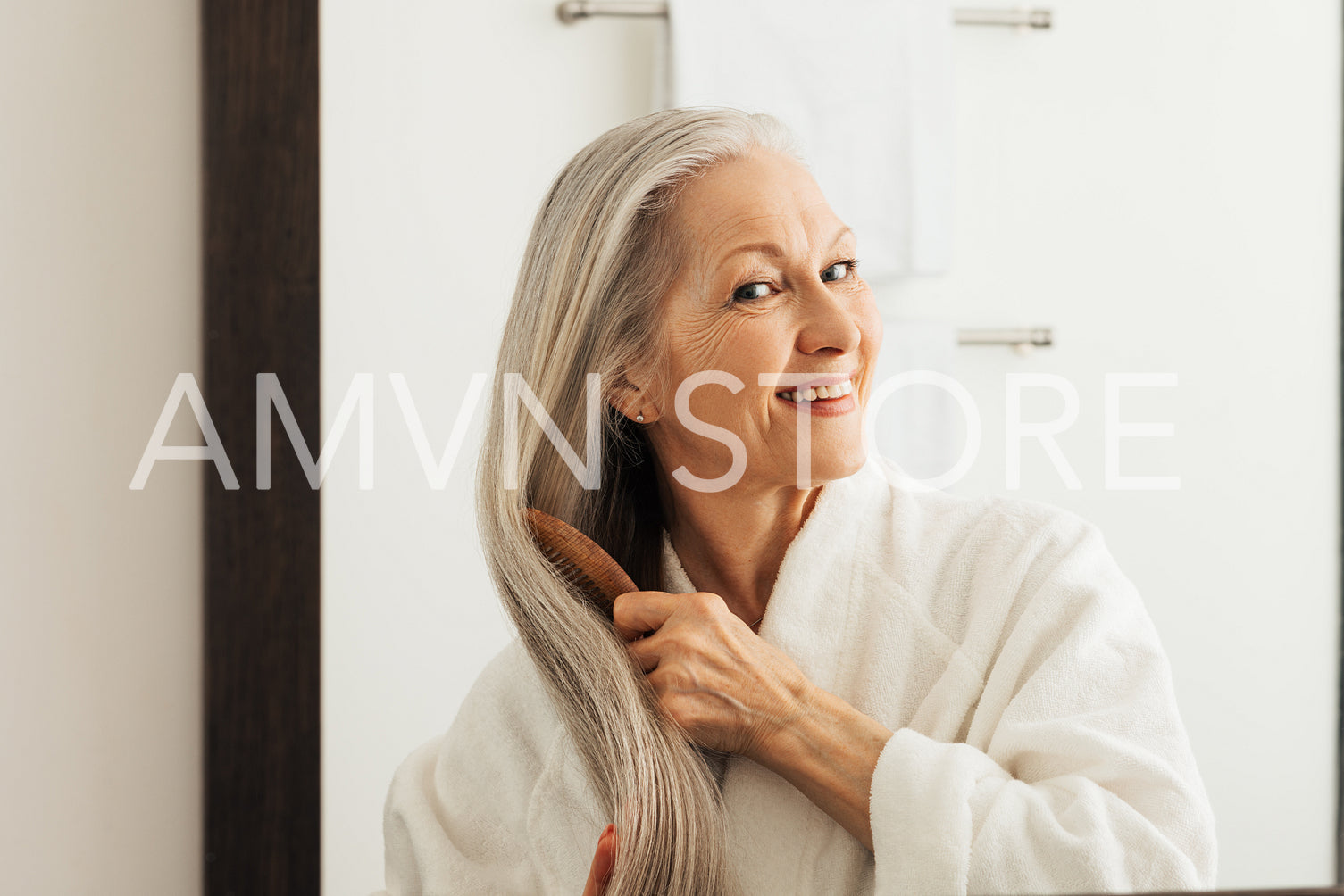 Smiling woman combing her long gray hair in front of a mirror