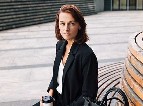 Middle-aged business woman sitting outdoors during lunch holding coffee