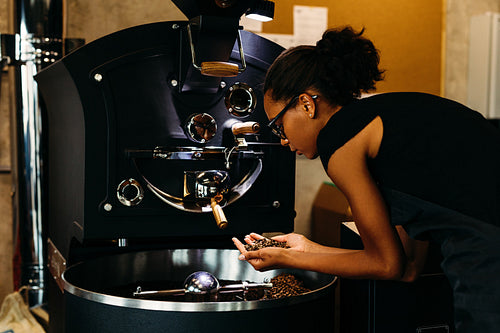 Young barista checking coffee beans in roasting machine, standing in coffee shop