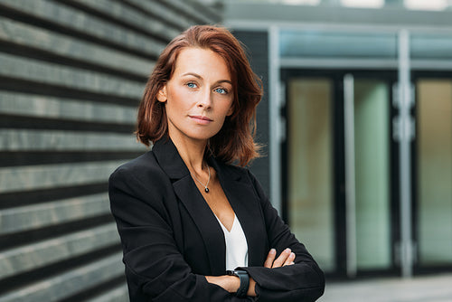 Portrait of a confident businesswoman with ginger hair. Middle-aged businesswoman standing with crossed arms outdoors.