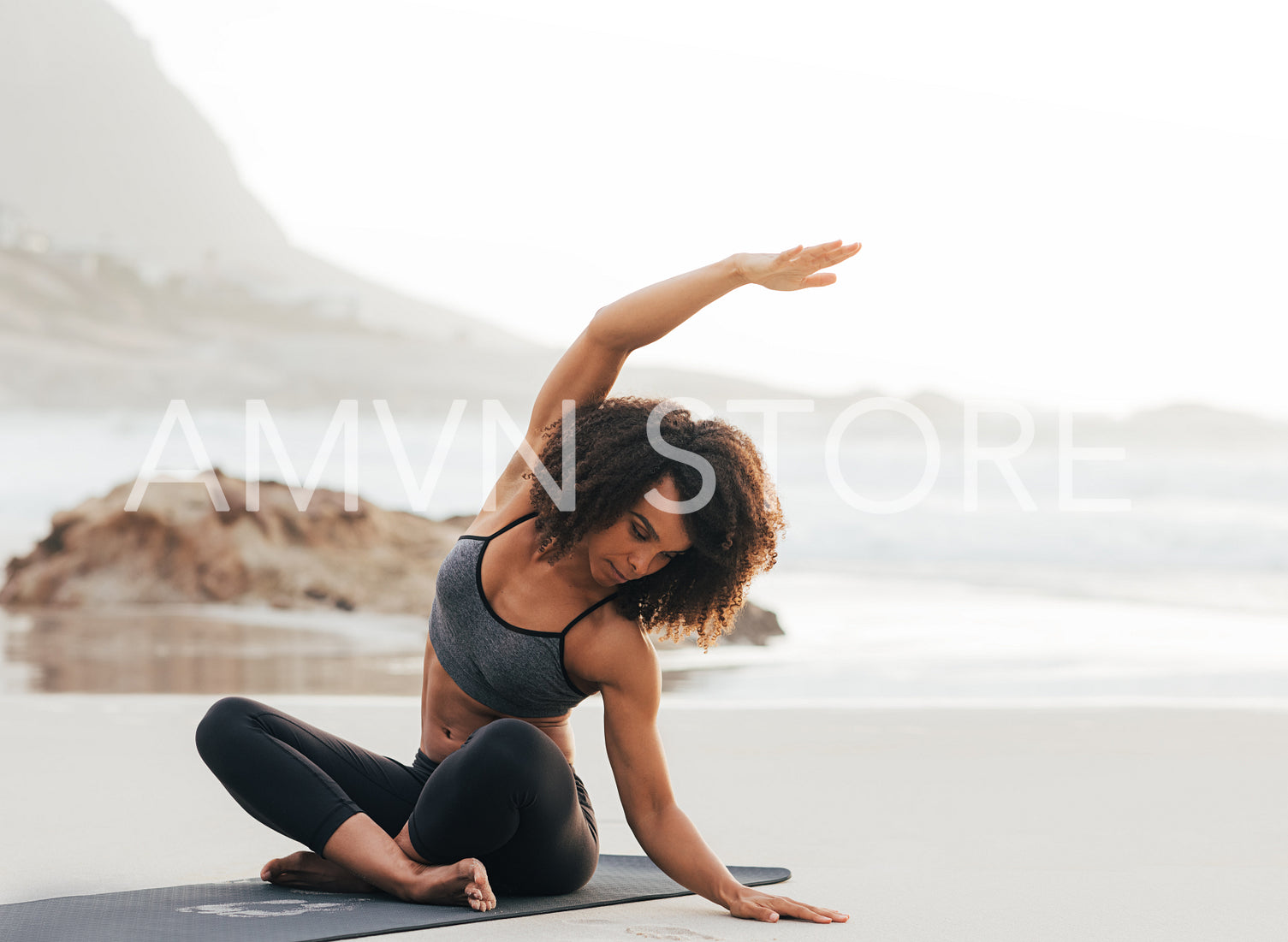 Young woman flexing her body while sitting on mat at beach 