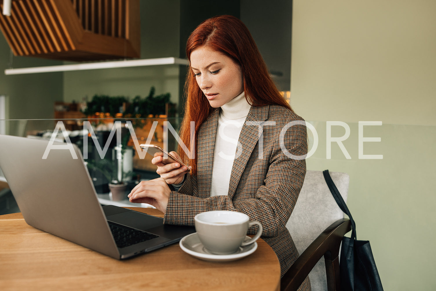 Woman with ginger hair holding a smartphone sitting at a cafe. Businesswoman working from the coffee shop.