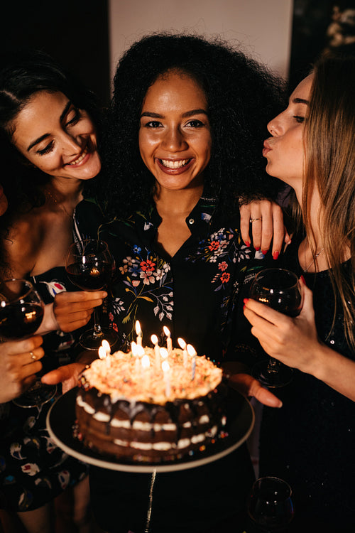 Young happy woman holding a birthday cake surrounded by friends