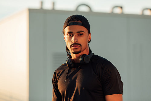 Portrait of a confident male athlete wearing a black cap, wireless headphones, and sports clothes looking at the camera