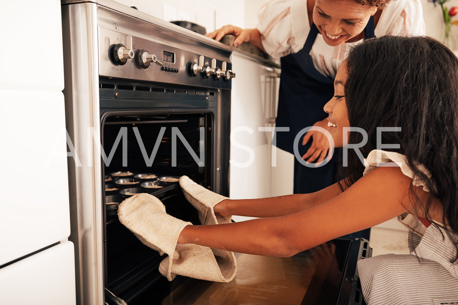 Granny and granddaughter putting unbaked cookies in oven. Girl wearing oven gloves putting cupcake molds.