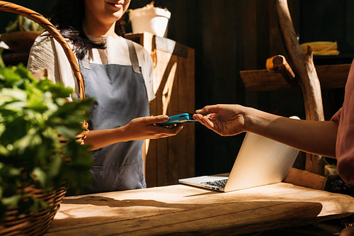 Vendor receiving payment from customer by card machine. Hands of unrecognizable women standing at a counter in an outdoor market and making a transaction.