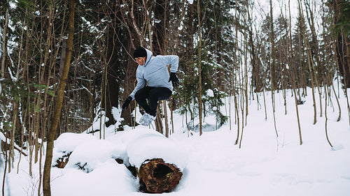 Young sportsman jumping through a tree in snowy forest