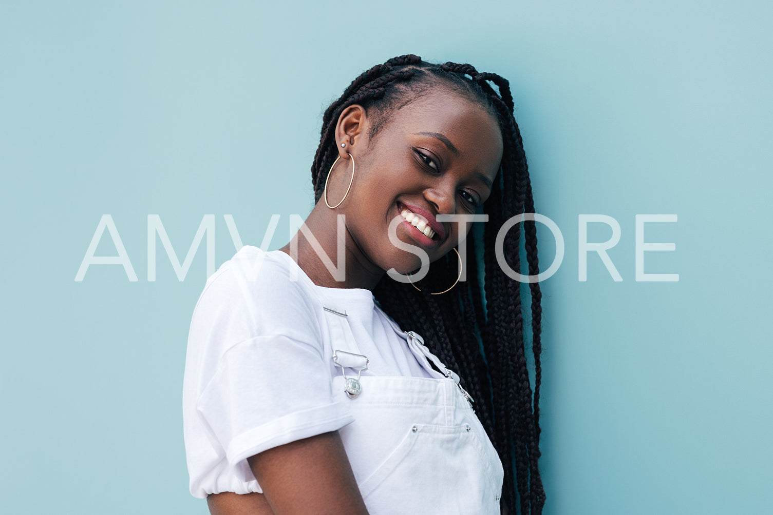 Portrait of young smiling woman with braids leaning on blue wall looking at camera