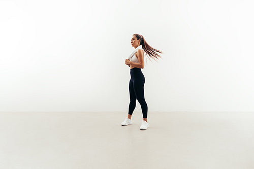 Young fit woman with white towel on her neck relaxing after workout indoors