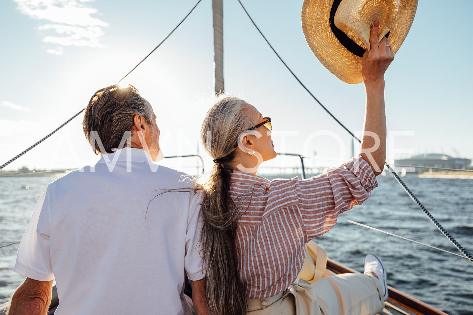 Back view of relaxed mature couple sitting on yacht. Stylish woman waving hat during boat trip.	