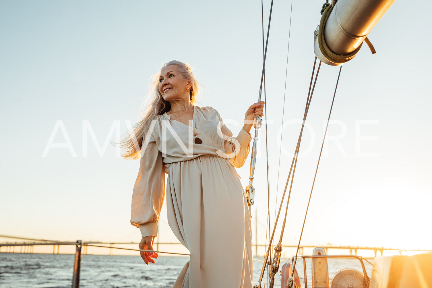 Attractive senior female in long dress looking away outdoors. Caucasian mature woman standing on a sailboat deck.	