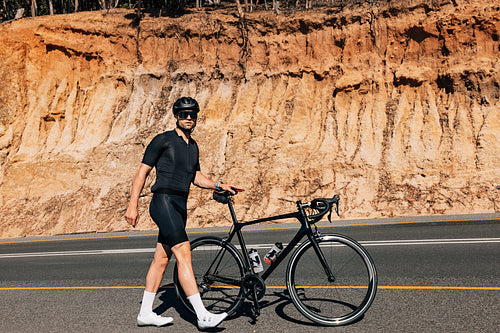 Professional male cyclist walking with his road bike and looking away