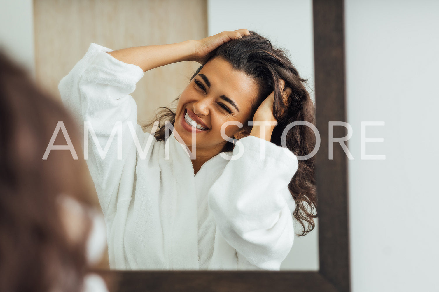 Happy brunette woman with palms in her hair looking at mirror reflection in the bathroom	